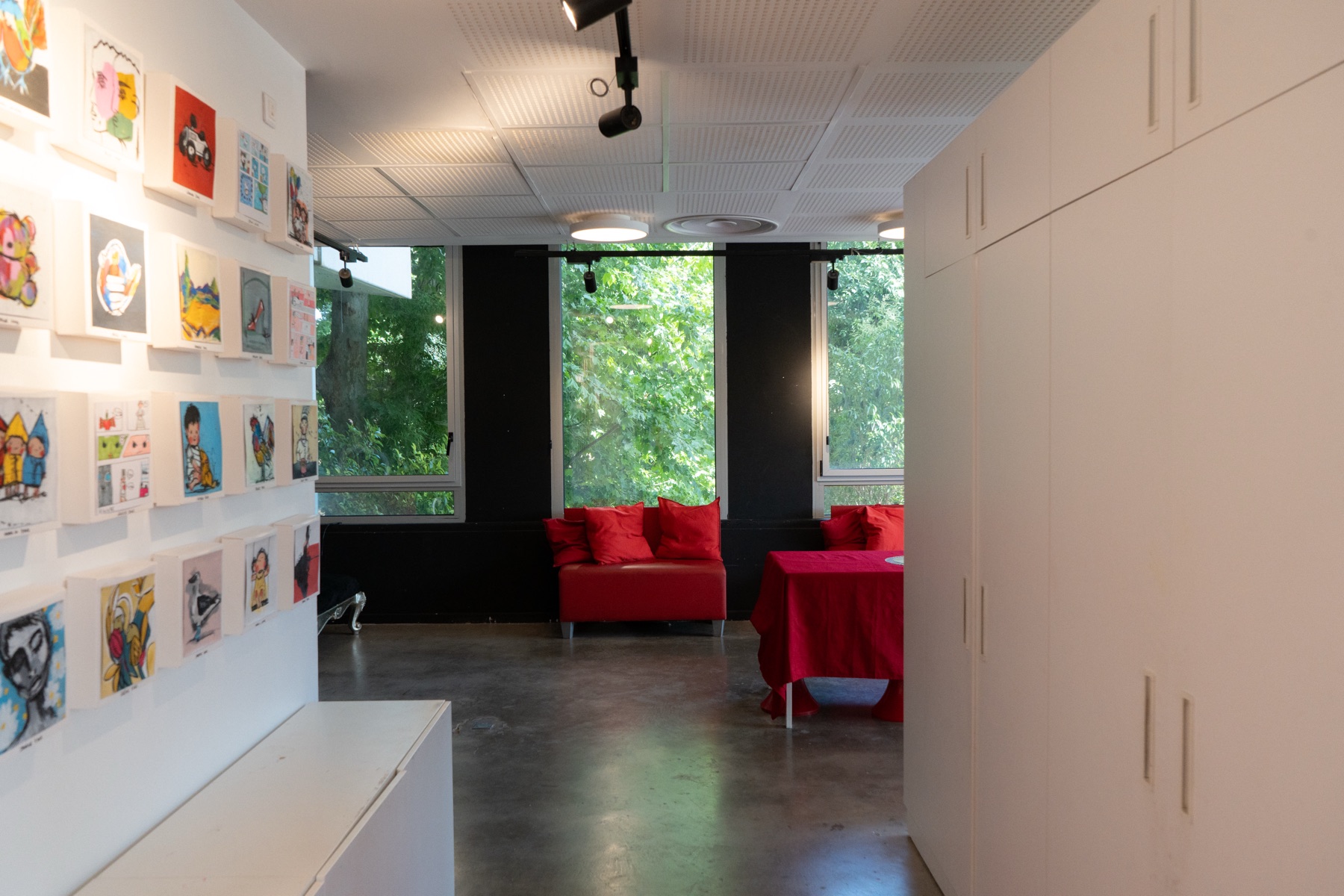 Le mur d’œuvres de l’espace blanc, en enfilade vers les fauteuils et les baies.